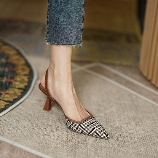 Checkered high-heeled shoes worn with rolled-up jeans on a textured floor.