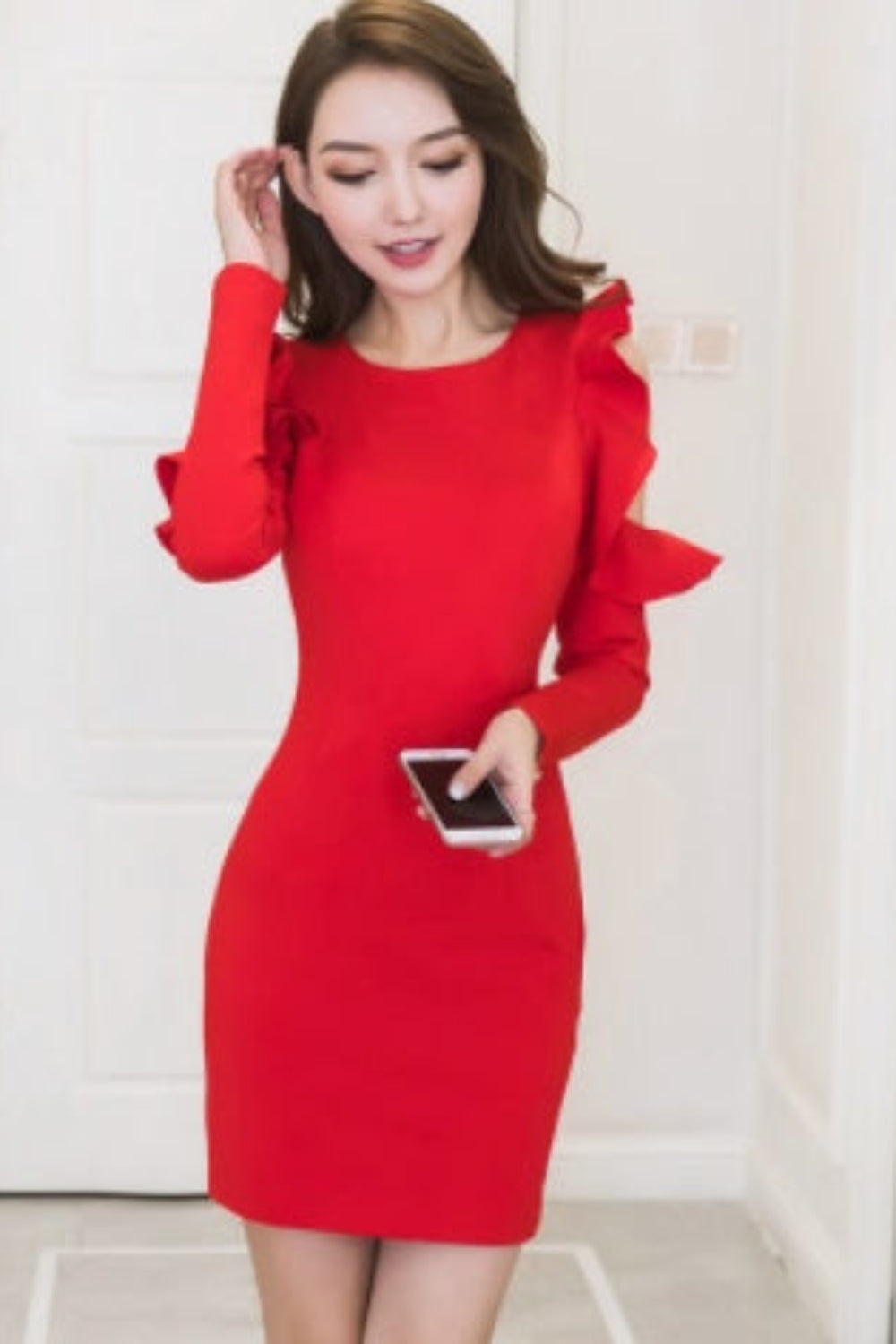 Woman wearing a red dress with ruffled sleeves in a minimal indoor setting.