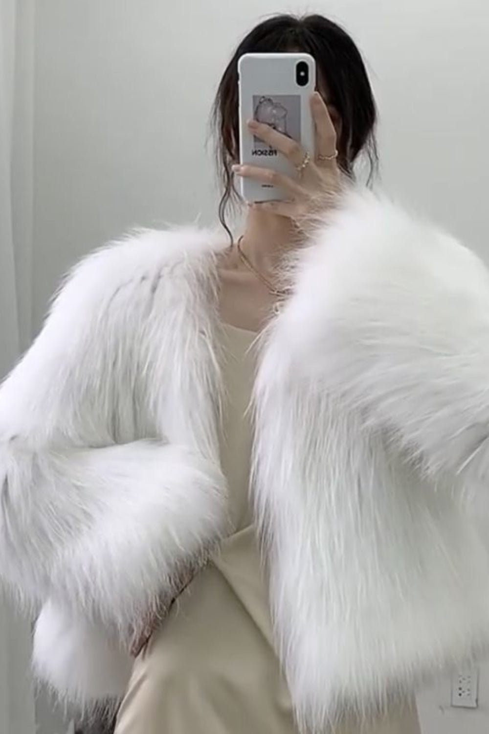 Person wearing a white fluffy coat taking a mirror selfie.