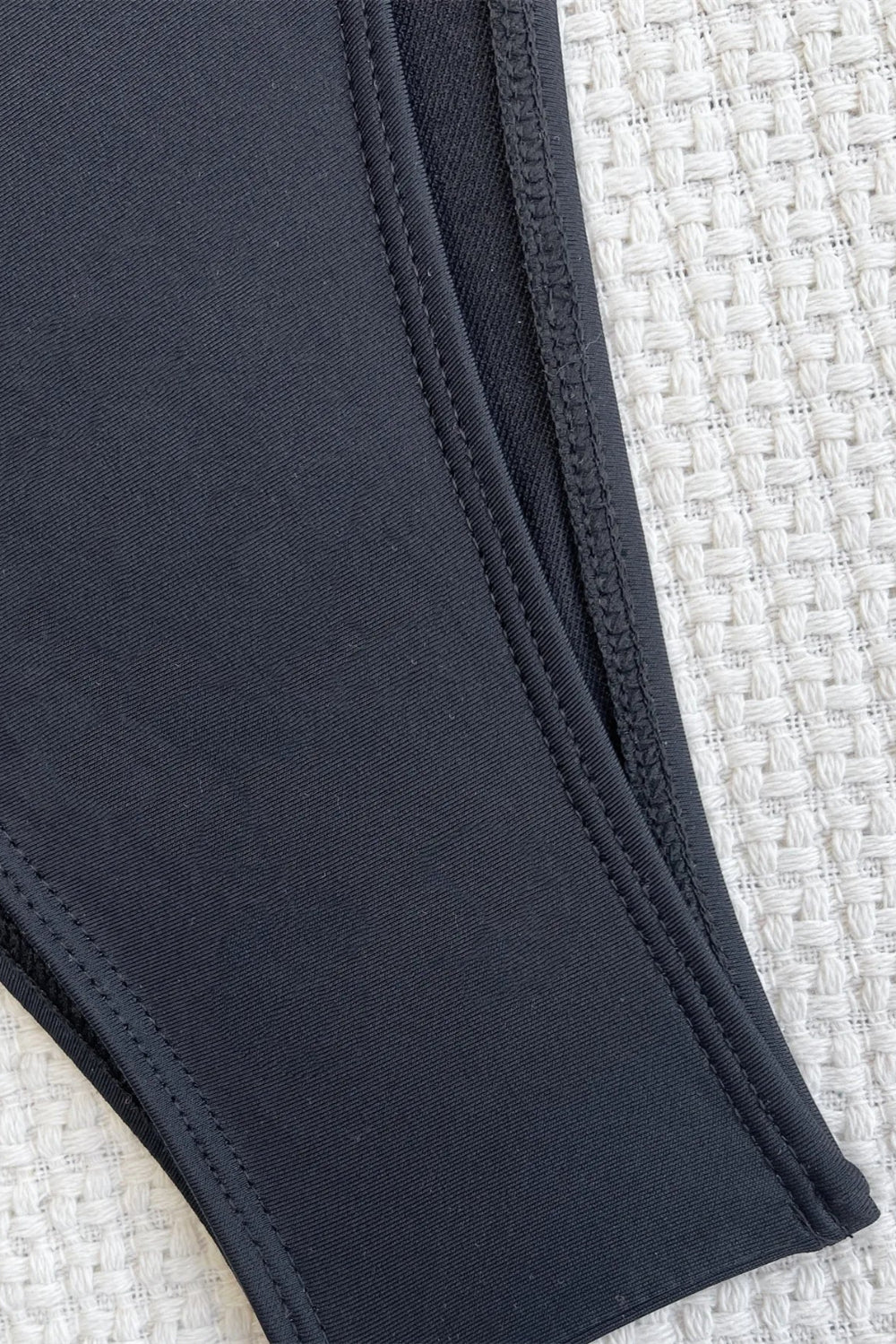 Close-up of a dark blue fabric with stitching detail on a textured beige background