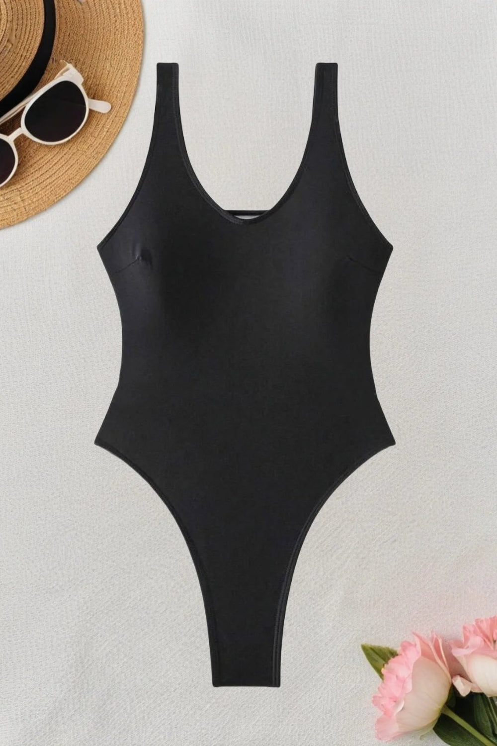 Black swimsuit on a light background with a straw hat and sunglasses.