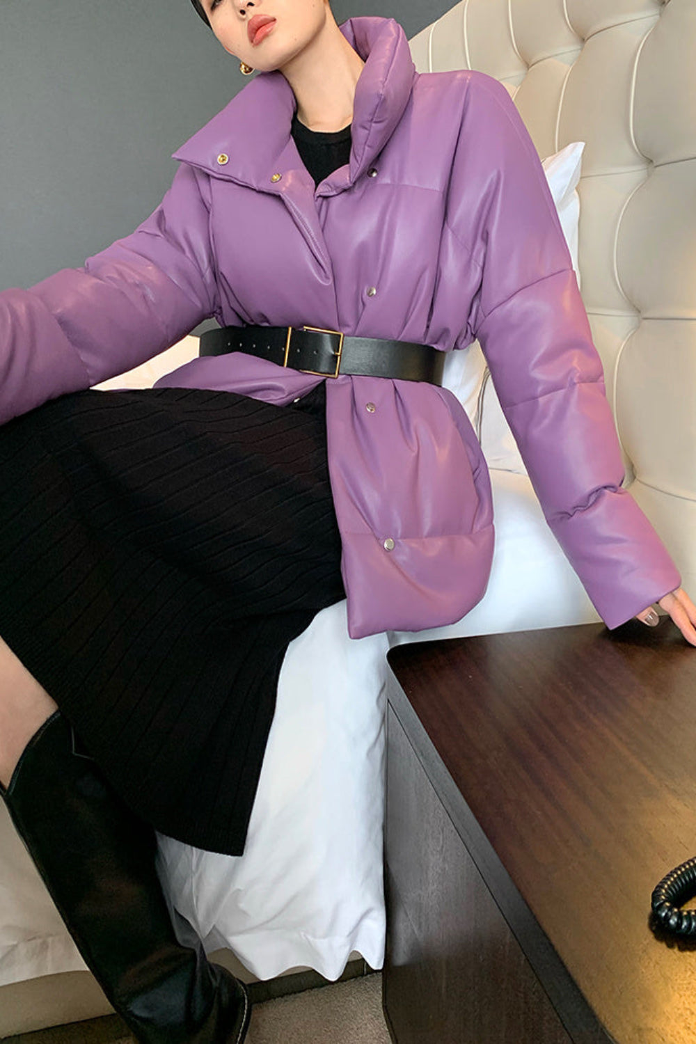 Person wearing a purple puffer jacket sitting on a bed.