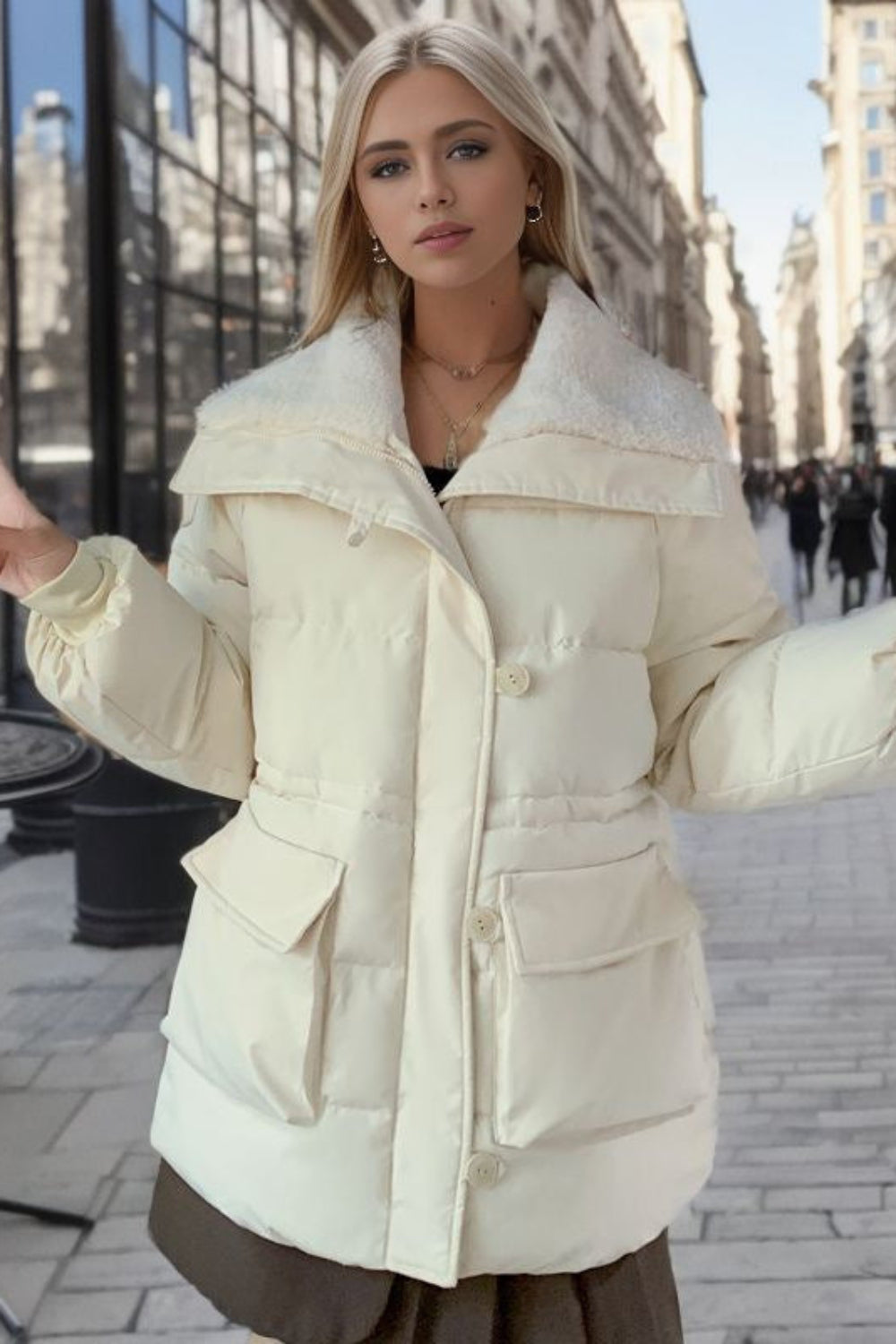 Woman in a cream puffer jacket holding a coffee cup on a city street.