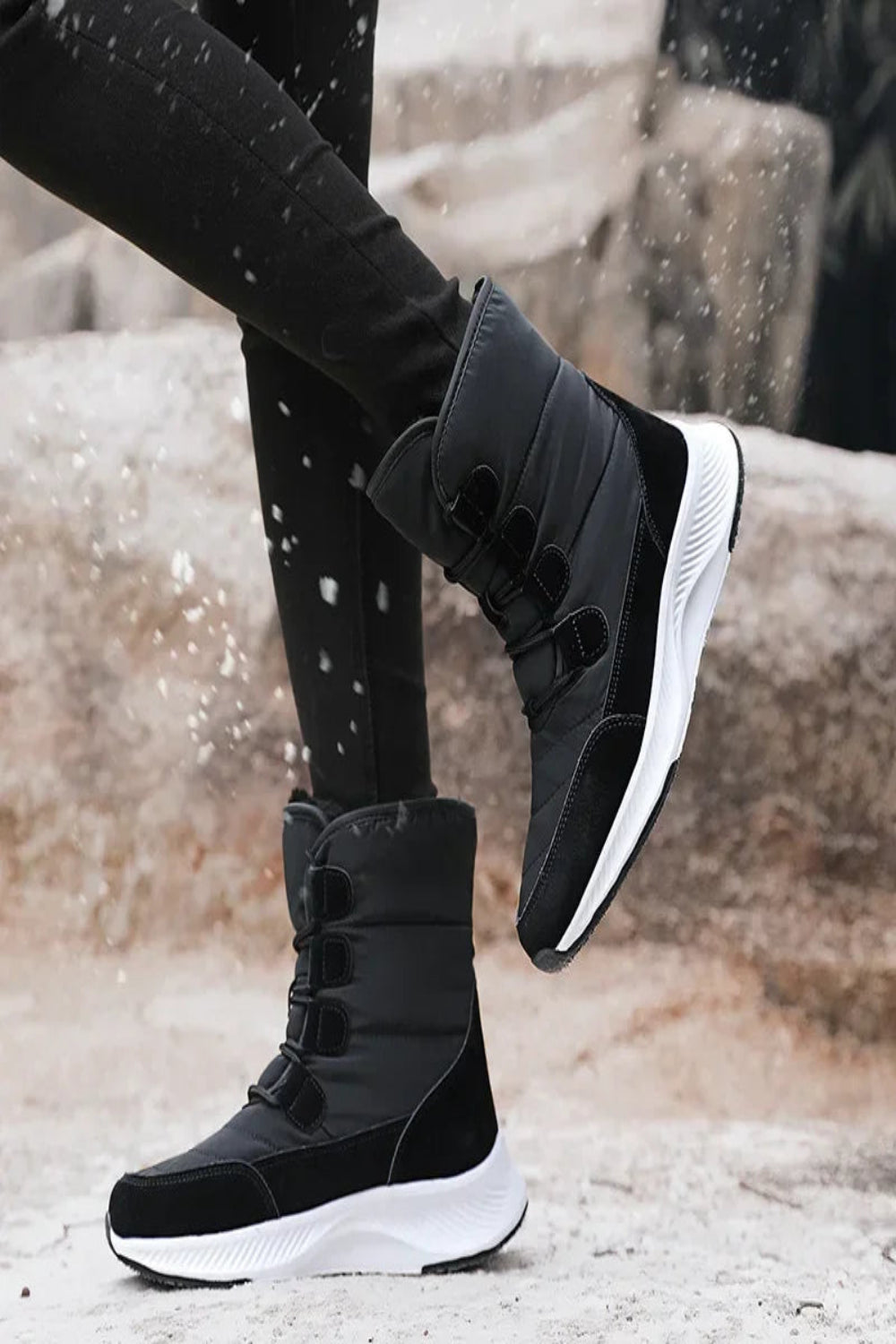 Black winter boots with white soles worn by a person on a snowy ground.
