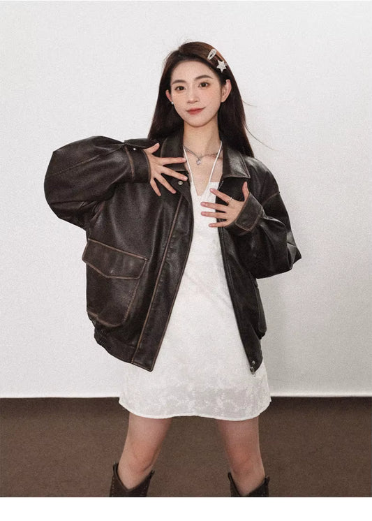 Woman wearing a black leather jacket over a white dress against a plain background