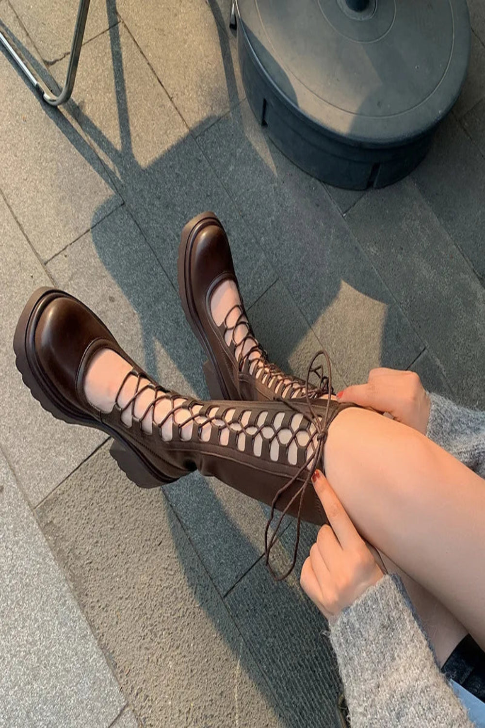 Person wearing brown lace-up boots on a pavement.