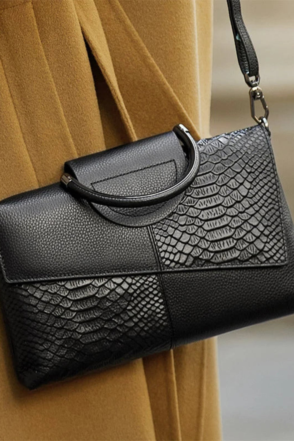 Black textured handbag with a patterned flap over a beige coat.