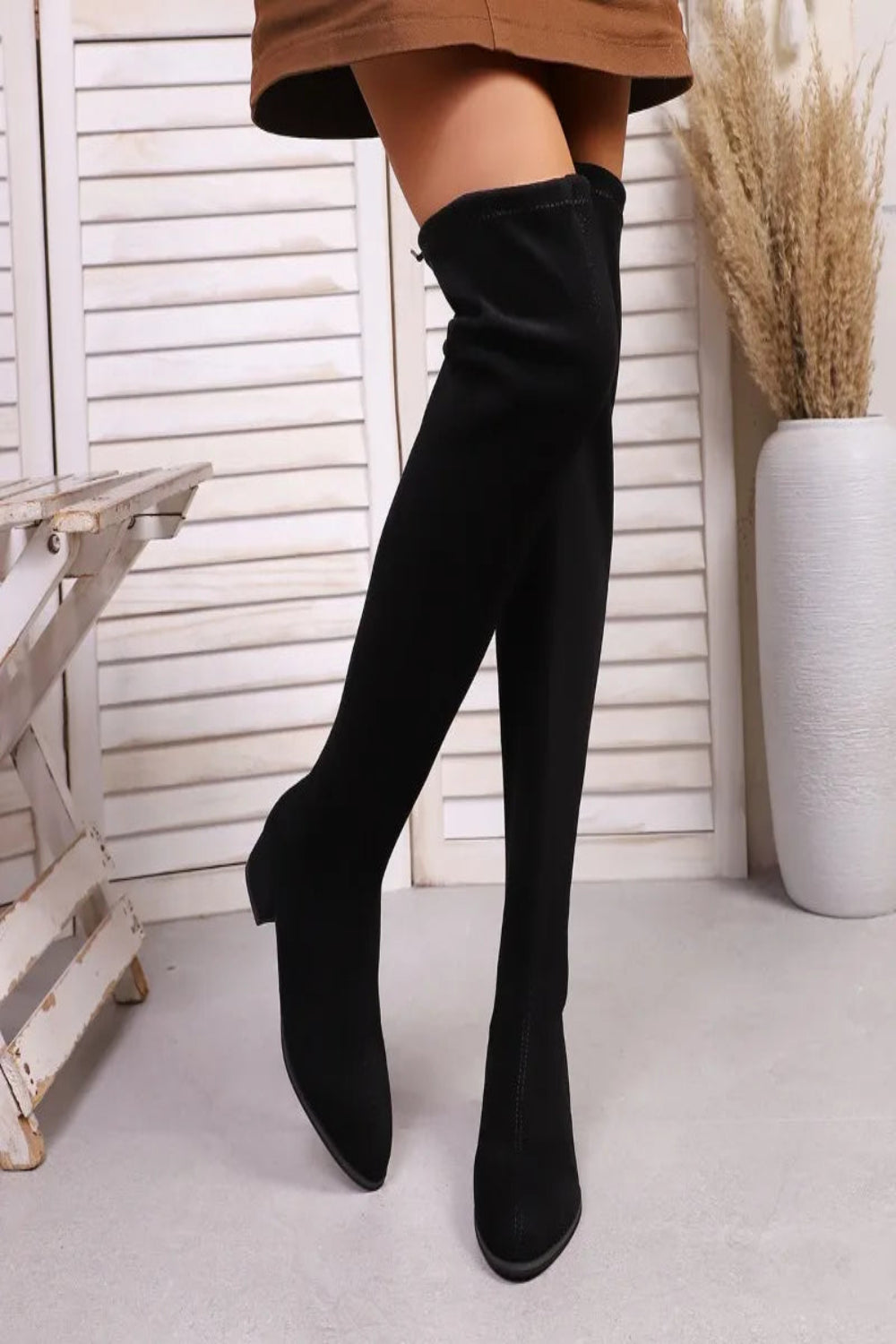 Black knee-high boots worn with a brown skirt against a white background