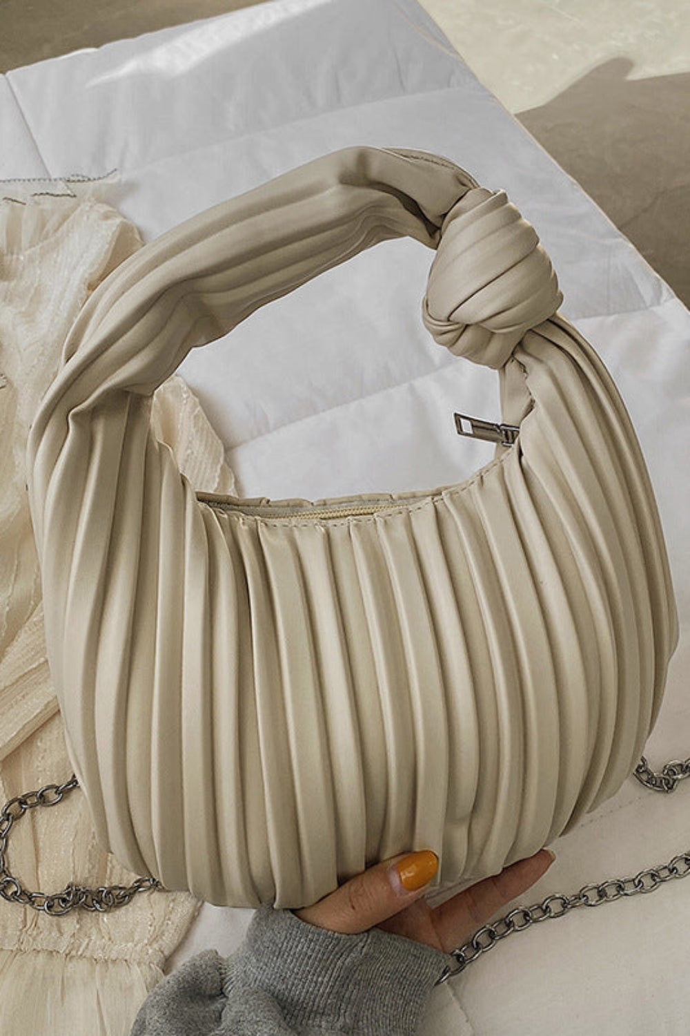 Beige pleated handbag with a chain detail held by a hand on a light background