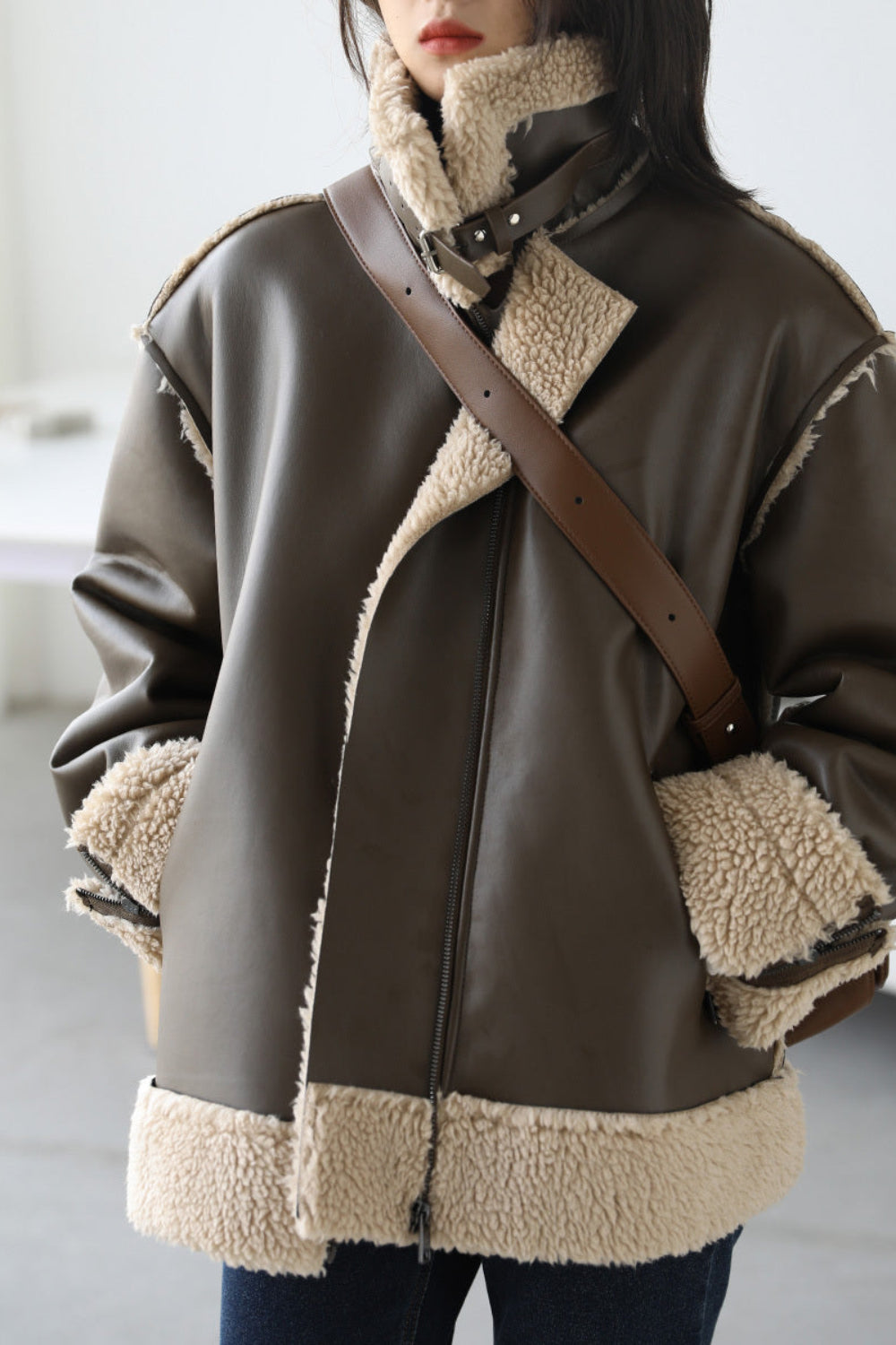Person wearing a brown leather jacket with shearling trim indoors
