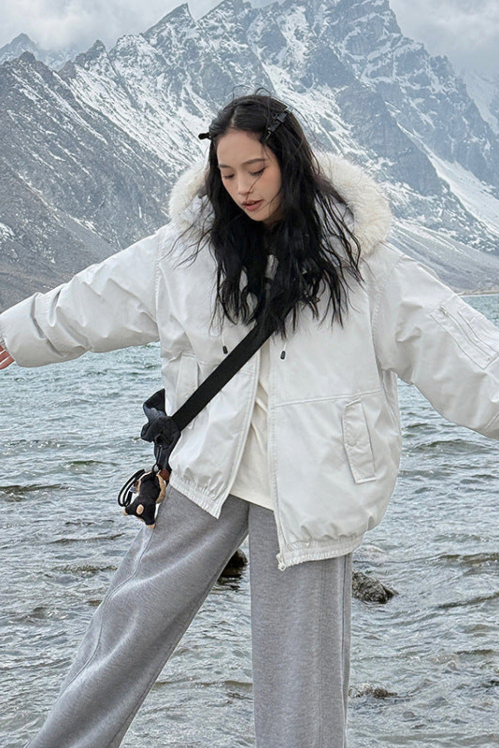 Person wearing a white coat with a fur-lined hood standing in front of a mountainous landscape.