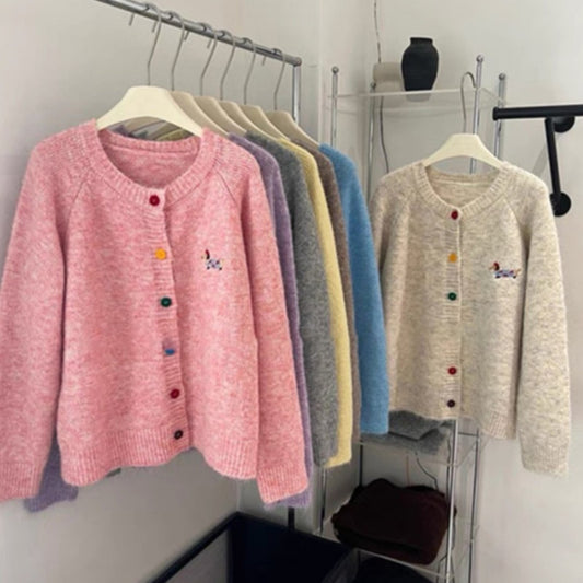 Row of colorful cardigans hanging on a rack against a white wall.