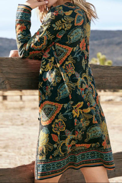 Woman wearing a patterned dress standing by a wooden fence with a scenic background