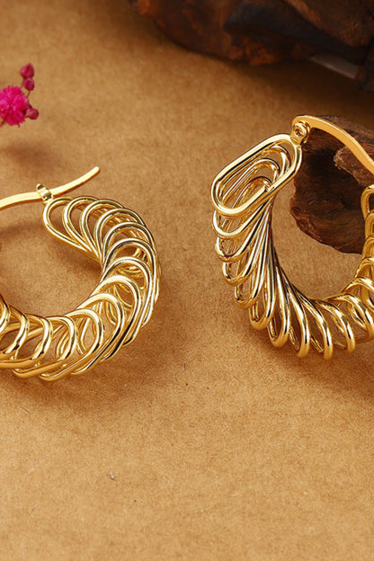 Gold hoop earrings on a brown surface with pink flowers in the background