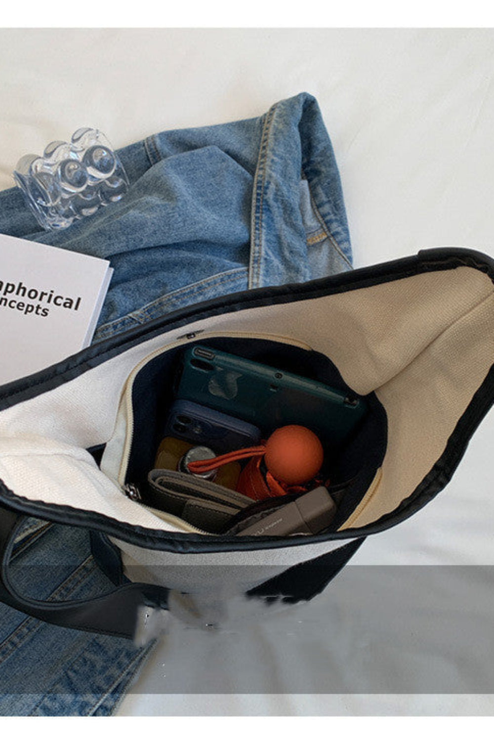 Open bag with denim jacket, book, and various items on a light gray background