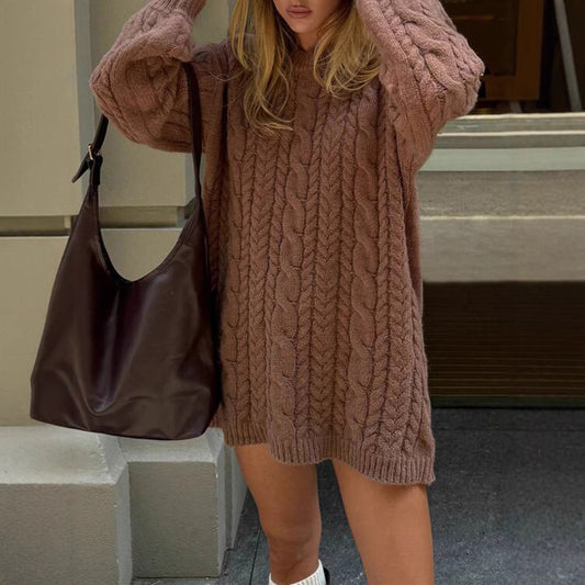 Person wearing a cable knit sweater and holding a brown bag on a street.