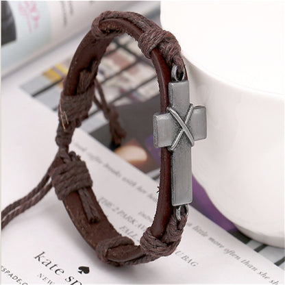 Brown braided leather bracelet with a silver cross charm on a magazine background