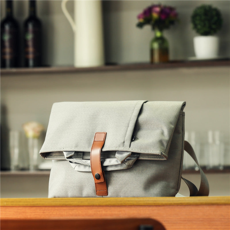 Gray bag with a brown strap on a wooden surface, blurred background