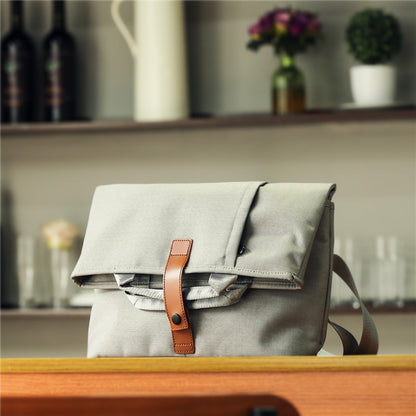 Gray bag with a brown strap on a wooden surface, blurred background