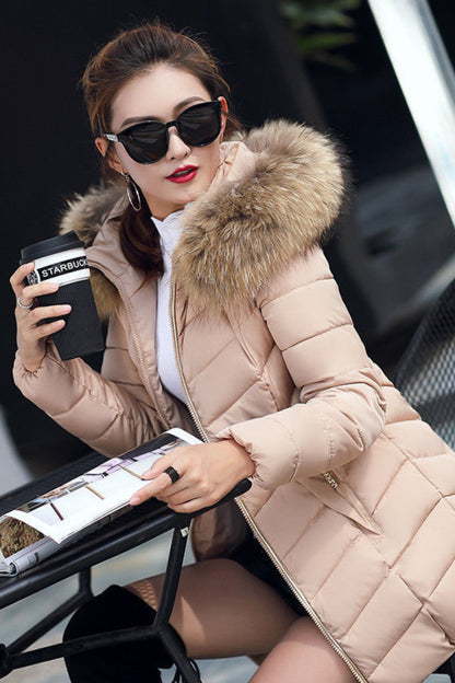 Woman in a beige puffer jacket with fur hood, holding a Starbucks cup and reading a magazine outdoors.