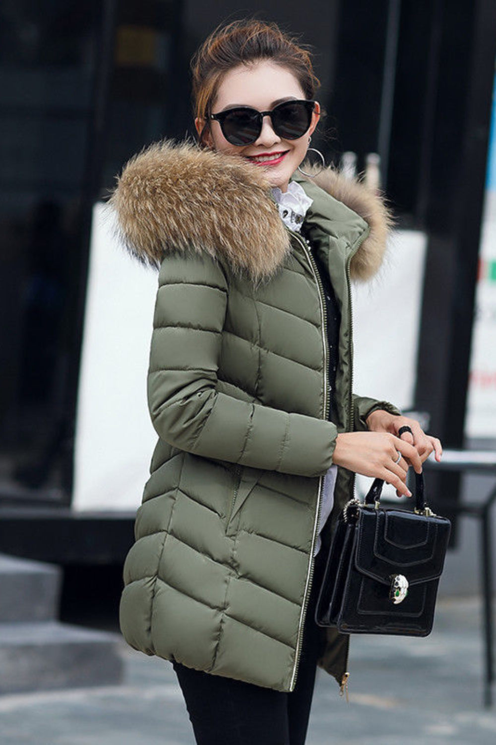 Woman wearing a green puffer jacket with a fur-lined hood, holding a black handbag.