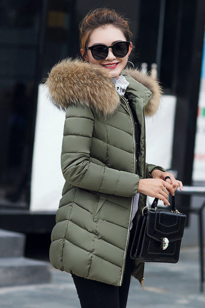 Woman wearing a green puffer jacket with a fur-lined hood, holding a black handbag.