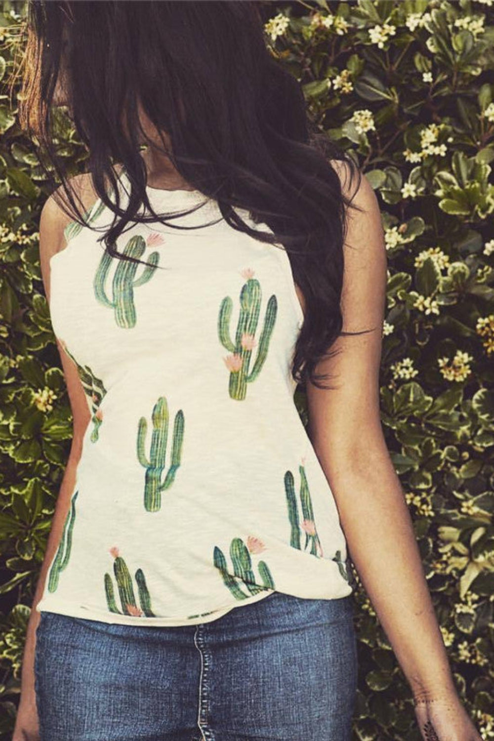 Person wearing a sleeveless top with cactus design in front of a green leafy background