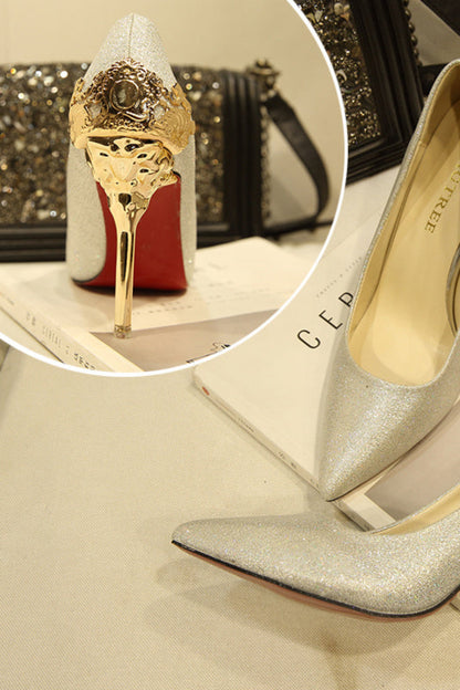 Silver high-heeled shoes with gold decorative heel on a textured surface.