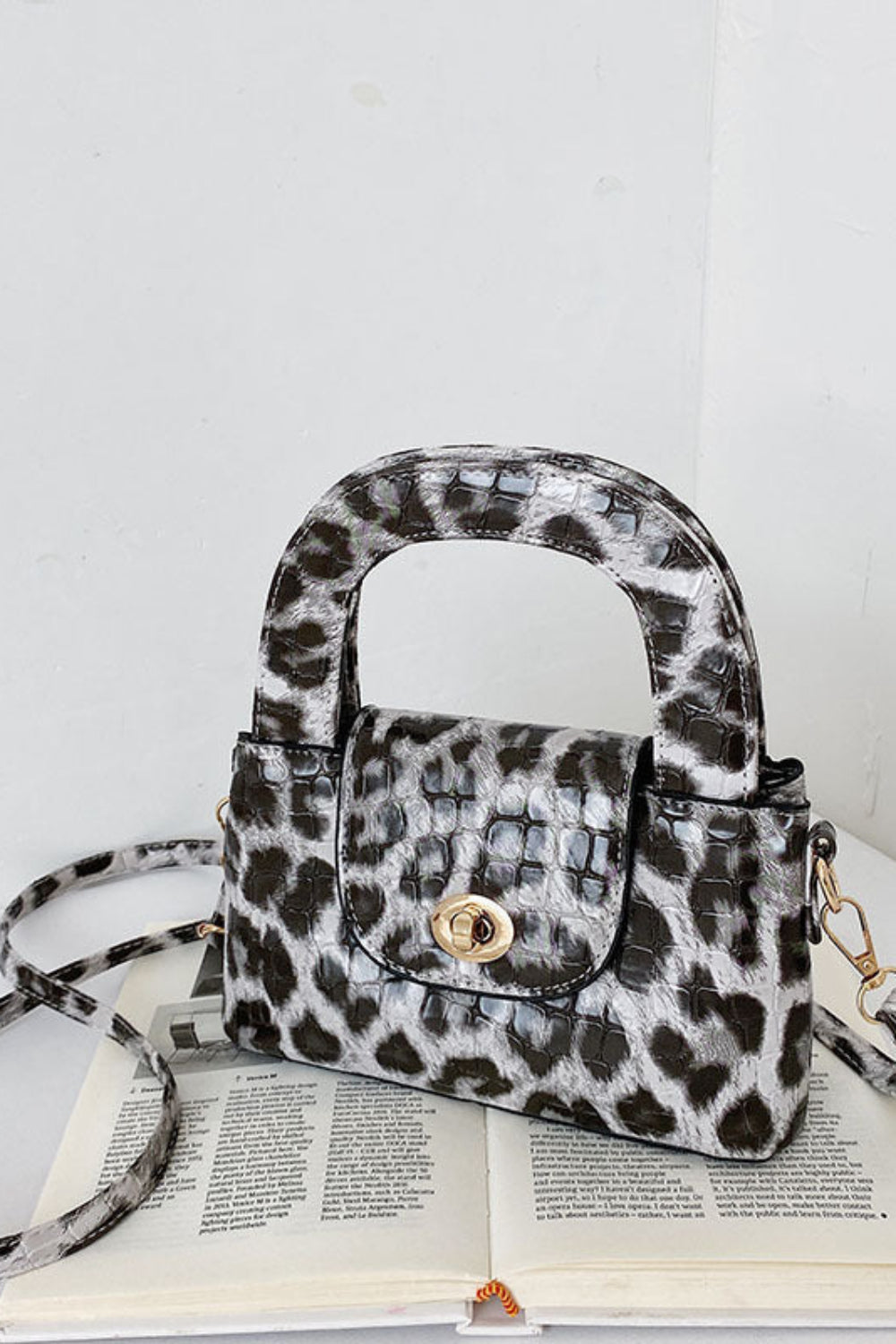 Leopard print handbag with a matching strap on an open book against a white background