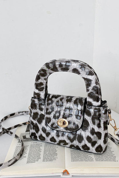 Leopard print handbag with a matching strap on an open book against a white background