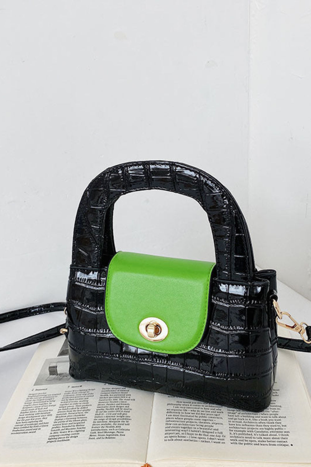 Black crocodile-patterned handbag with a green section on an open book against a white background