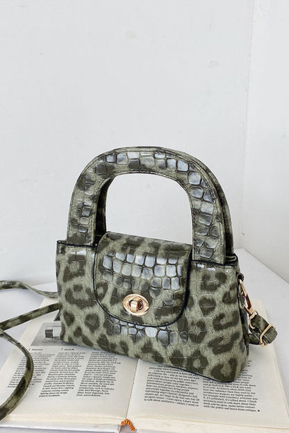 Green leopard print handbag with studded details on a white surface.
