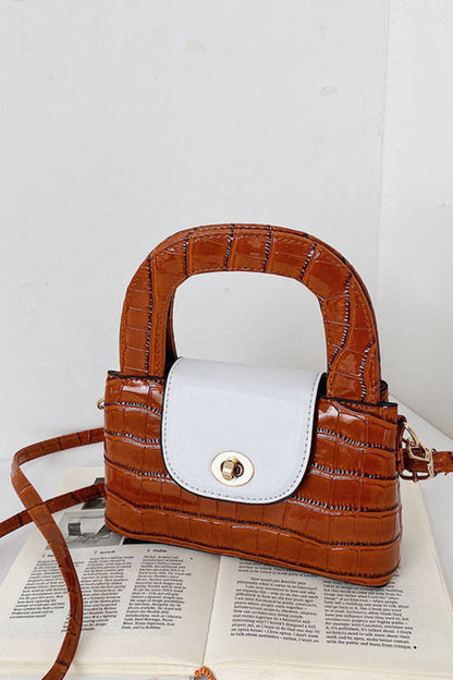 Brown crocodile-patterned handbag with white interior on an open book against a white background