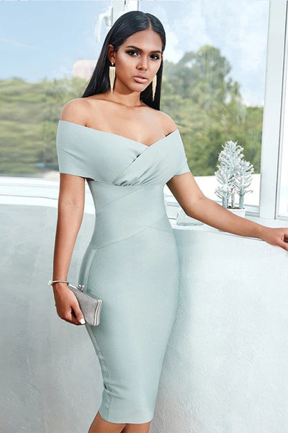 Woman in a light blue off-shoulder dress standing indoors with large windows.