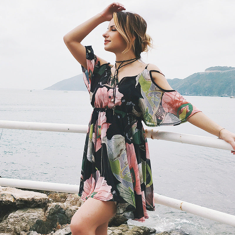 Woman in a floral dress standing by a waterfront with mountains in the background
