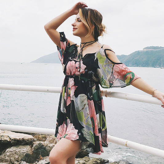 Woman in a floral dress standing by a waterfront with mountains in the background