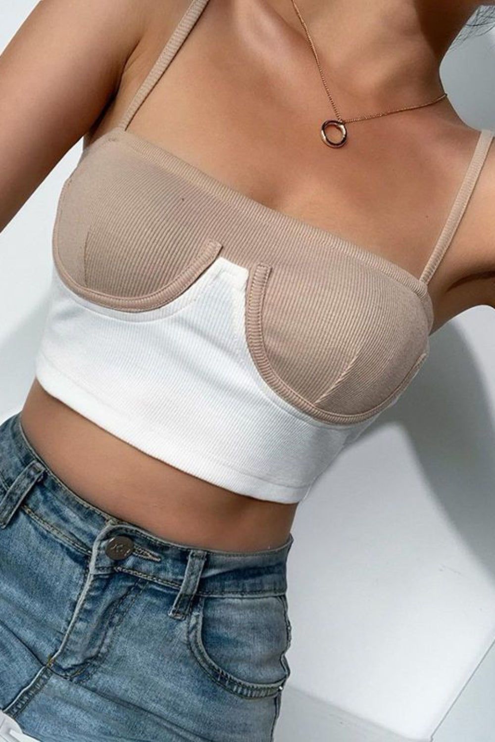 Person wearing a beige bra over a white crop top and blue jeans on a light background
