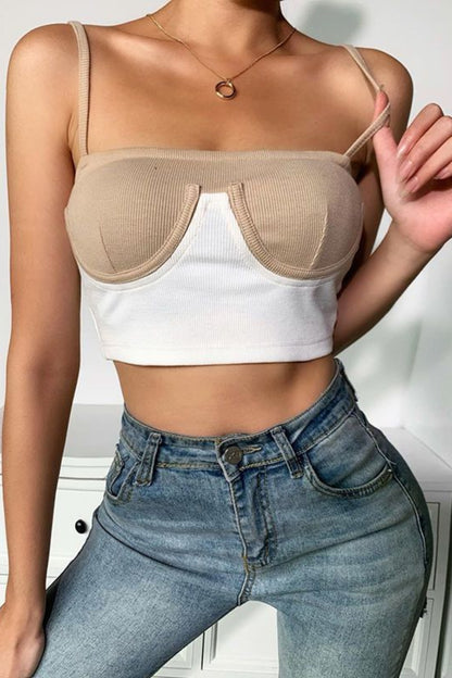 Person wearing a beige bralette over a white crop top and blue jeans indoors.