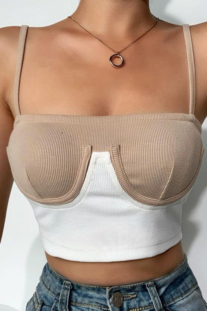 Person wearing a beige bralette over a white crop top with a plain background
