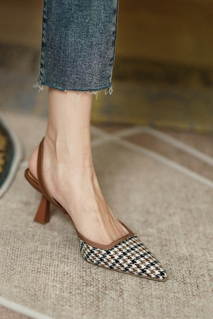 Checkered high-heeled shoes worn with rolled-up jeans on a textured floor.