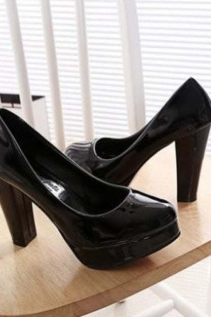 Black high-heeled shoes on a wooden surface with white blinds in the background