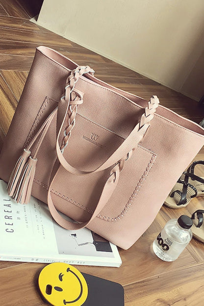 Pink handbag on a wooden floor with a book and water bottle nearby