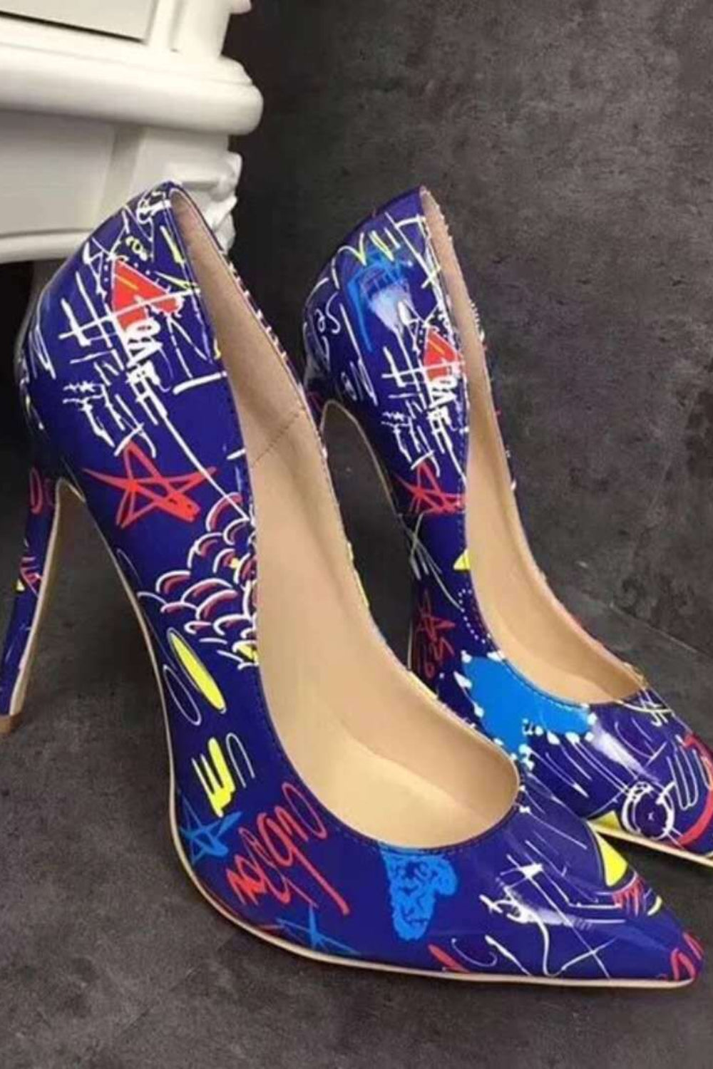 Pair of blue high-heeled shoes with colorful abstract patterns on a dark surface.