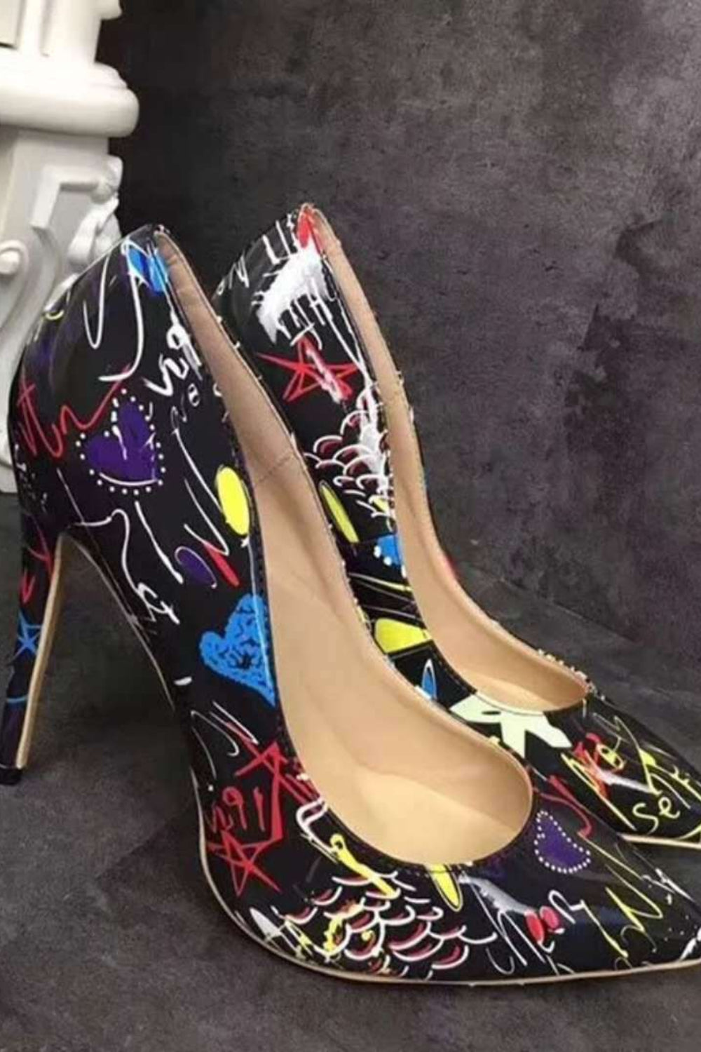 Pair of high-heeled shoes with colorful abstract designs on a dark surface.