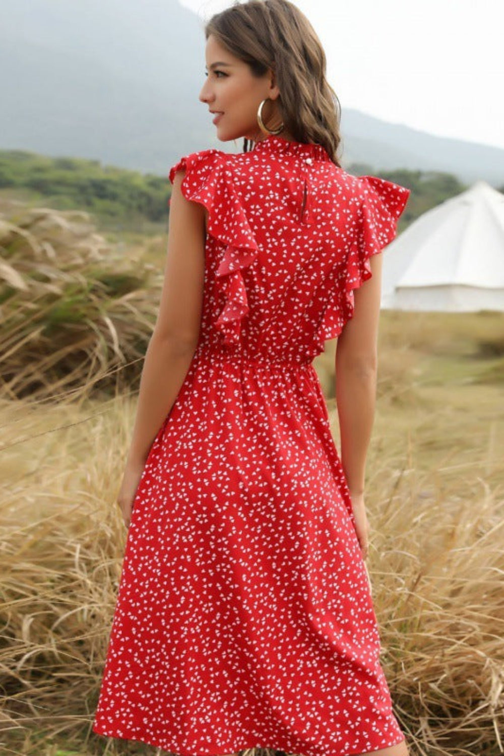 Woman in a red dress with white polka dots standing in a field with a tent in the background.