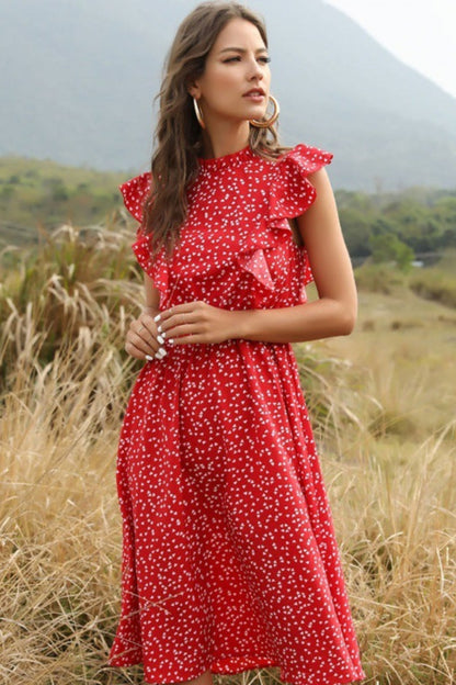 Woman in a red dress with white polka dots standing in a field with mountains in the background