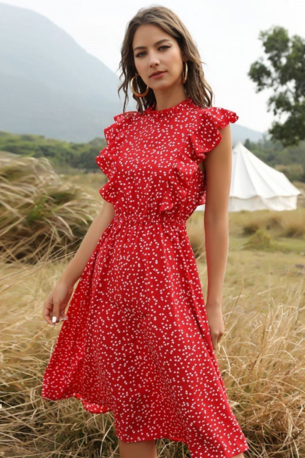 Woman in a red dress standing in a field with mountains in the background