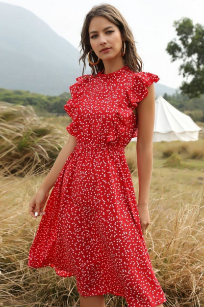 Woman in a red dress standing in a field with mountains in the background