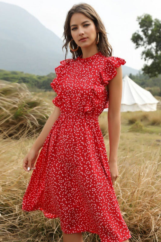 Woman in a red dress standing in a field with mountains in the background