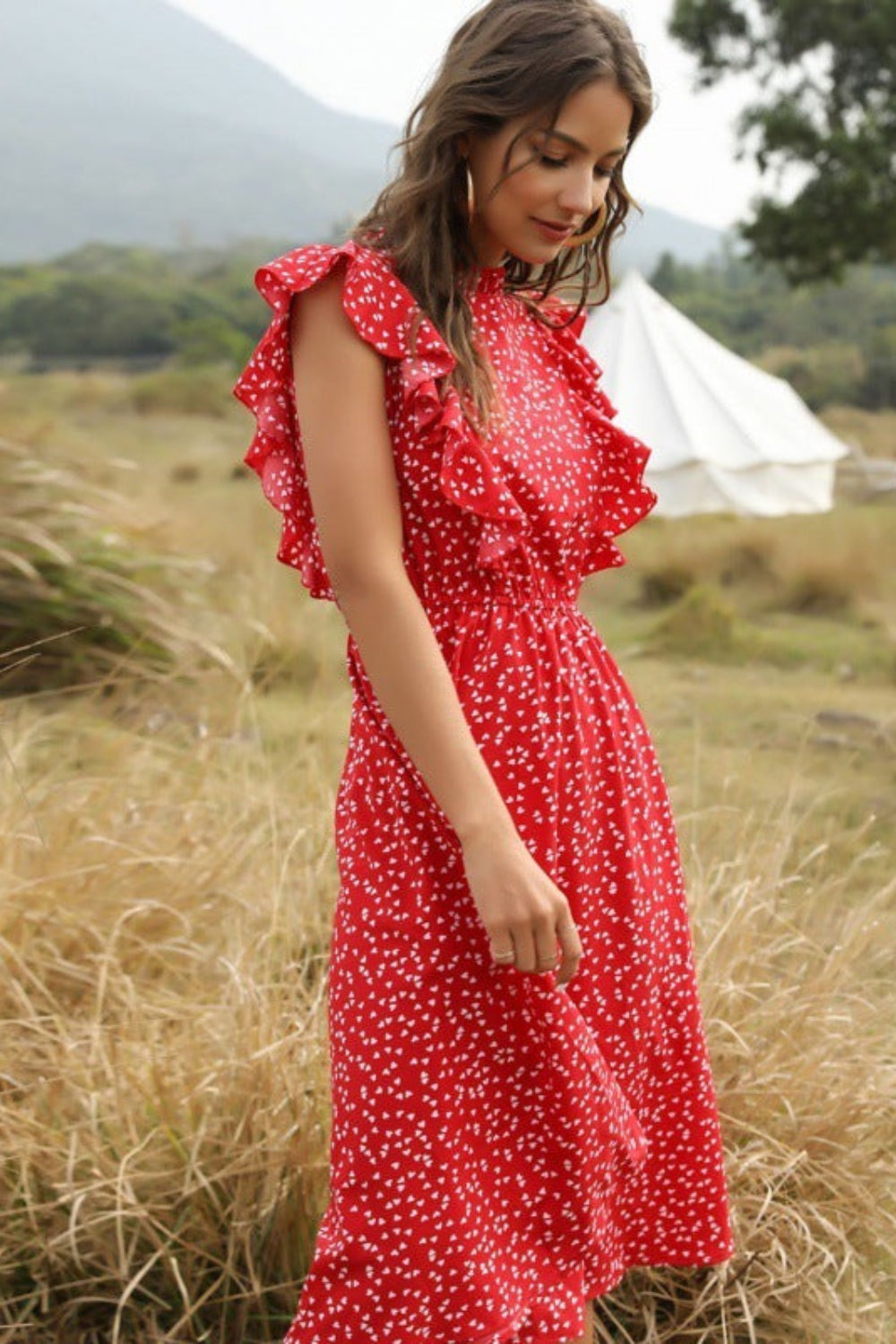 Woman in a red dress with white polka dots standing in a grassy field with a tent in the background.